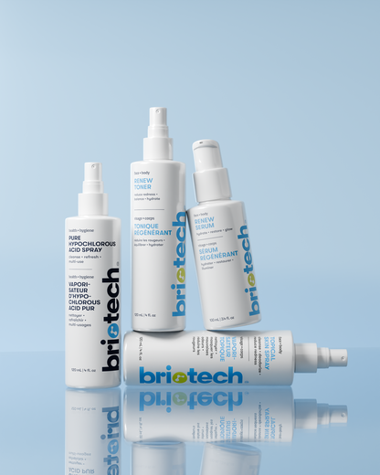 Four Briotech skincare products, including the Topical Skin Spray and serums, are arranged at various angles against a light blue background. The white bottles show blue and grey branding, formulated to calm irritation and reduce blemishes.